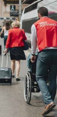 Un employé SNCF qui aide une personne en situation de handicap en poussant son fauteuil.
